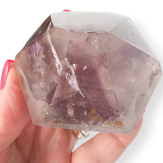 Purple Amethyst Crystal held in a hand with a white background