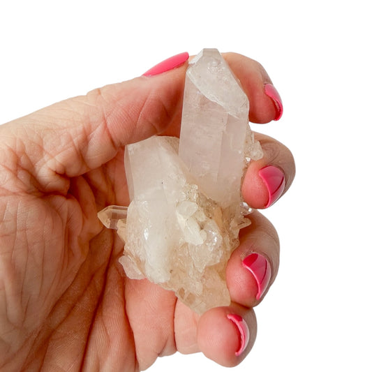 Hand holding a crystal with pink nail polish on a white background