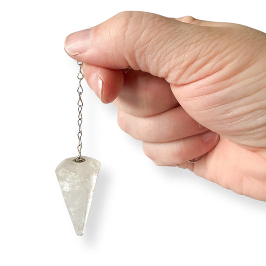 Hand holding golden rutile quartz pendulum against white background.