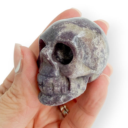 Hand holding a small lepidolite hand carved skull to show size and detail.