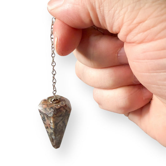 Hand holding a Sea Jasper pendulum on a white background