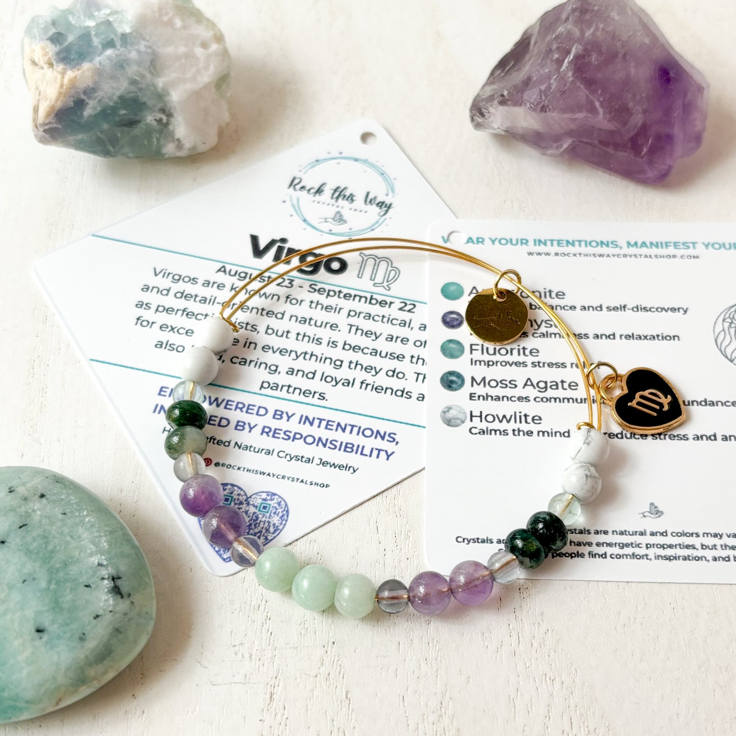 Virgo Flat Lay with Virgo Information Card, Gold Virgo Bracelet with Black Charm and Fluorite, Amethyst, and Amazonite Crystals.