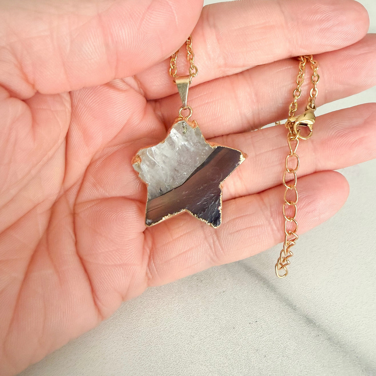 Close up of gold plated amethyst star pendant highlighting natural crystal texture and subtle purple coloring.