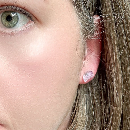 Close-up of amethyst crystal earrings worn on ear, unpolished natural stone