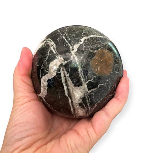 Hand holding Black Marble Sphere to show scale and smooth finish