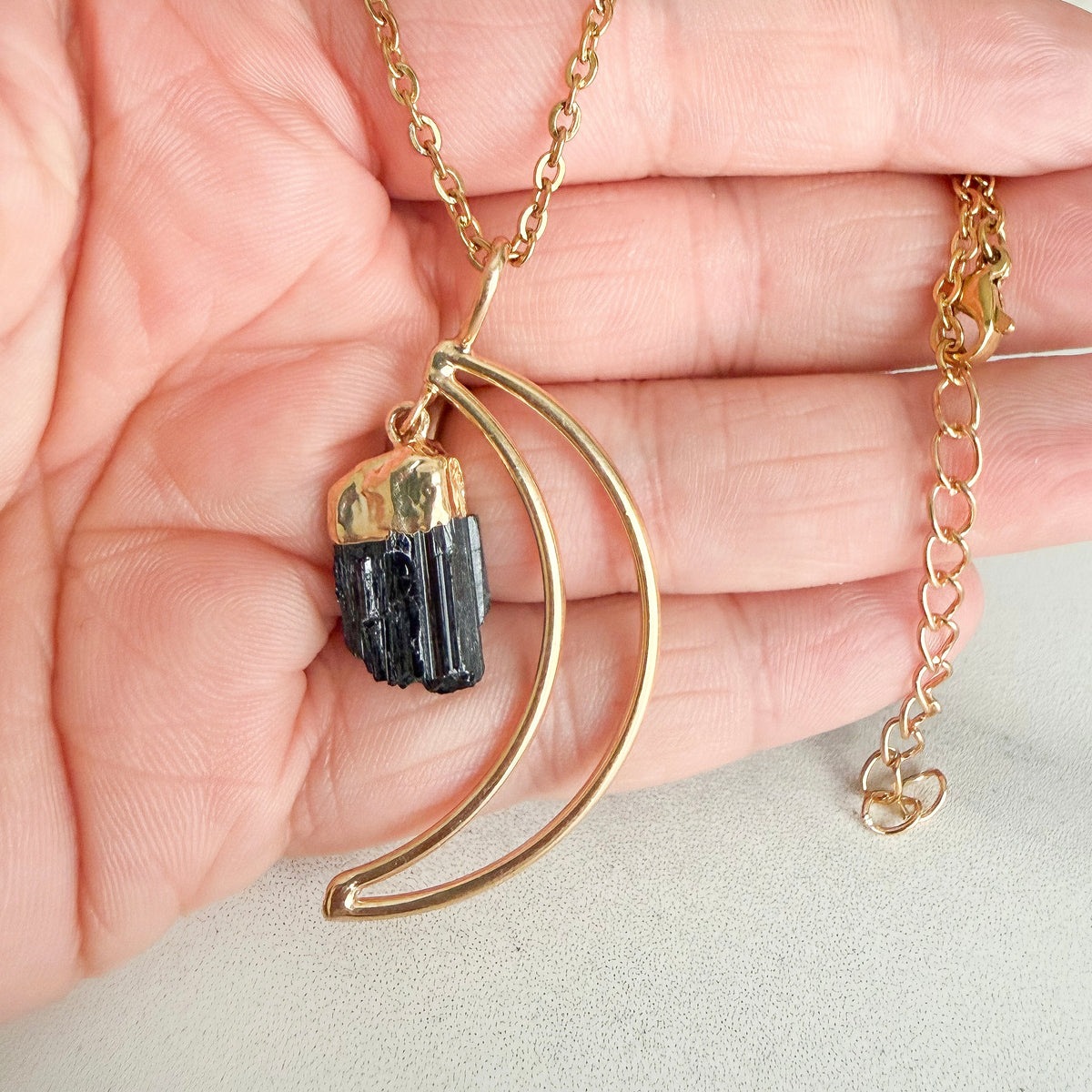 Natural black tourmaline crystal pendant with raw edges and deep black tones, suspended from a gold plated setting.