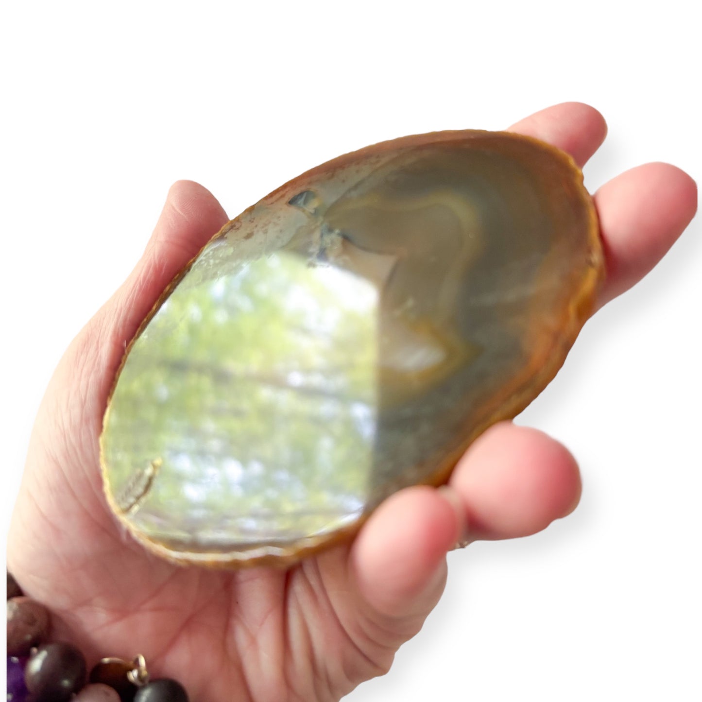 Hand holding brown and blue agate slice with visible color layers and sparkle