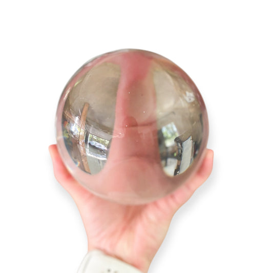 Clear glass gazing ball held in hand showing its size and reflective quality