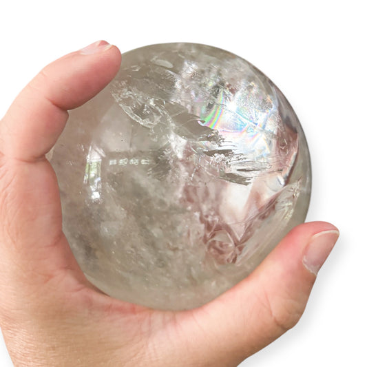 Hand holding a Clear Quartz crystal sphere with visible rainbows