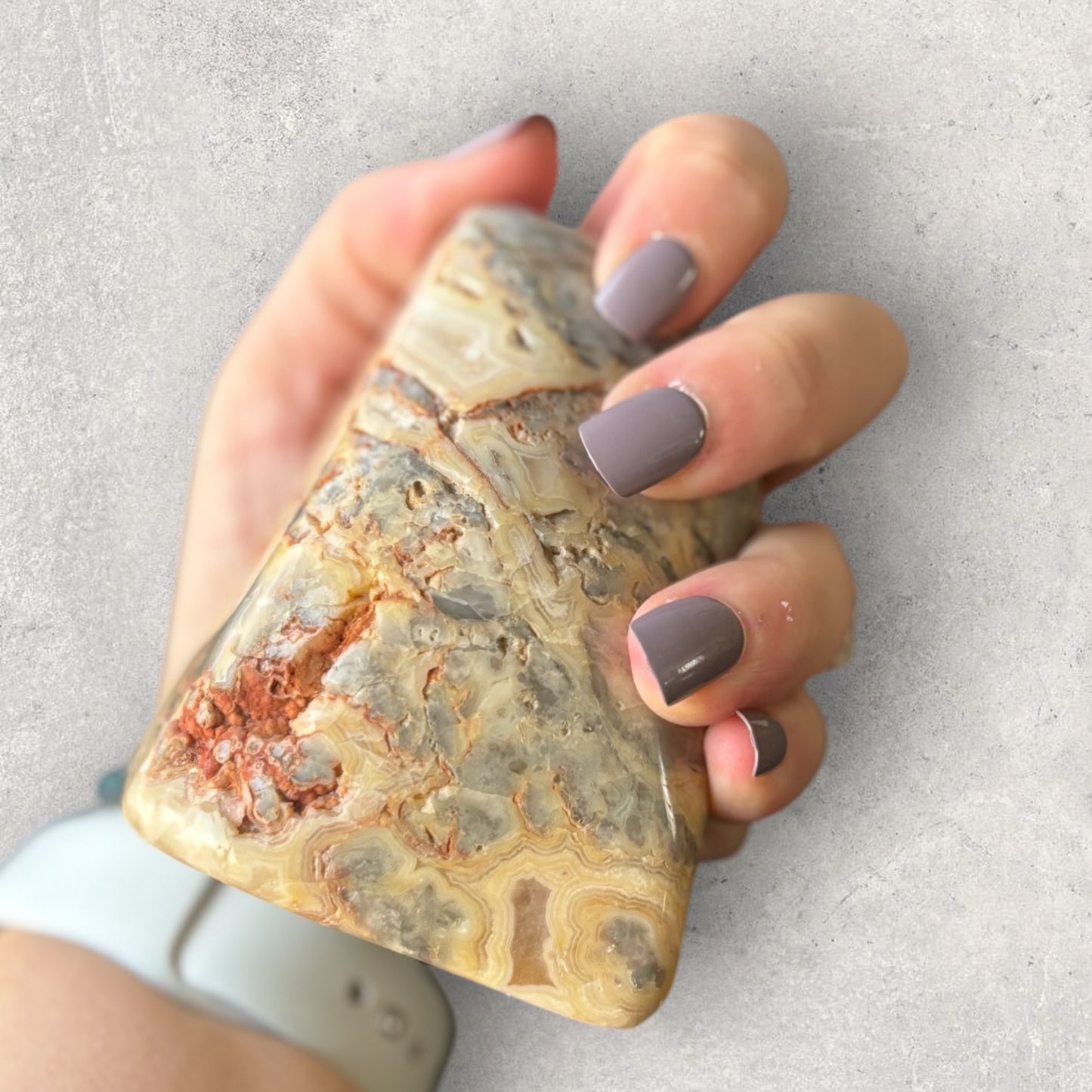 Close-up of Crazy Lace Agate with natural lines and warm earth tones in hand to show size reference