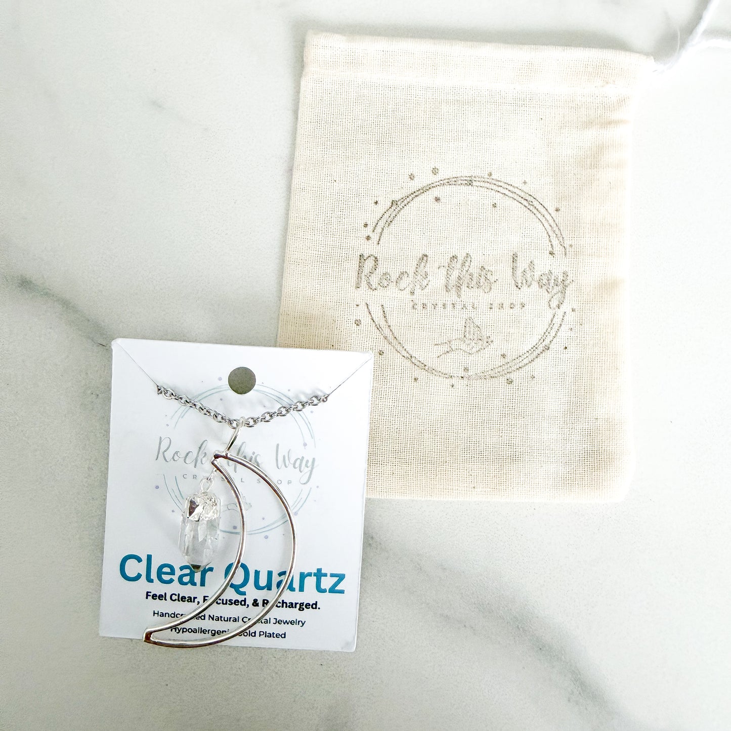Silver plated crescent moon with clear quartz pendant necklace displayed on Rock This Way Crystal Shop packaging with included polishing cloth.