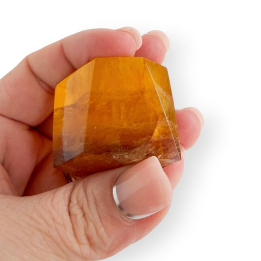 Polished Honey Fluorite freeform held in hand for size reference, featuring rich golden color and translucent crystal layers.