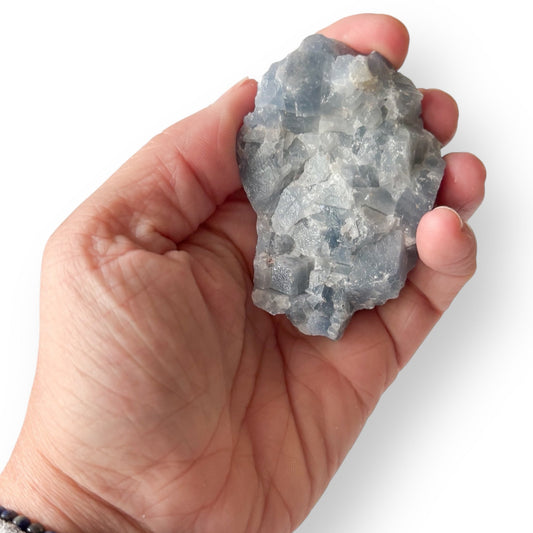 Hand holding Blue Calcite crystal to show natural size and color.