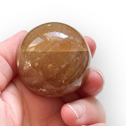 Honey Calcite crystal sphere held in hand for size reference