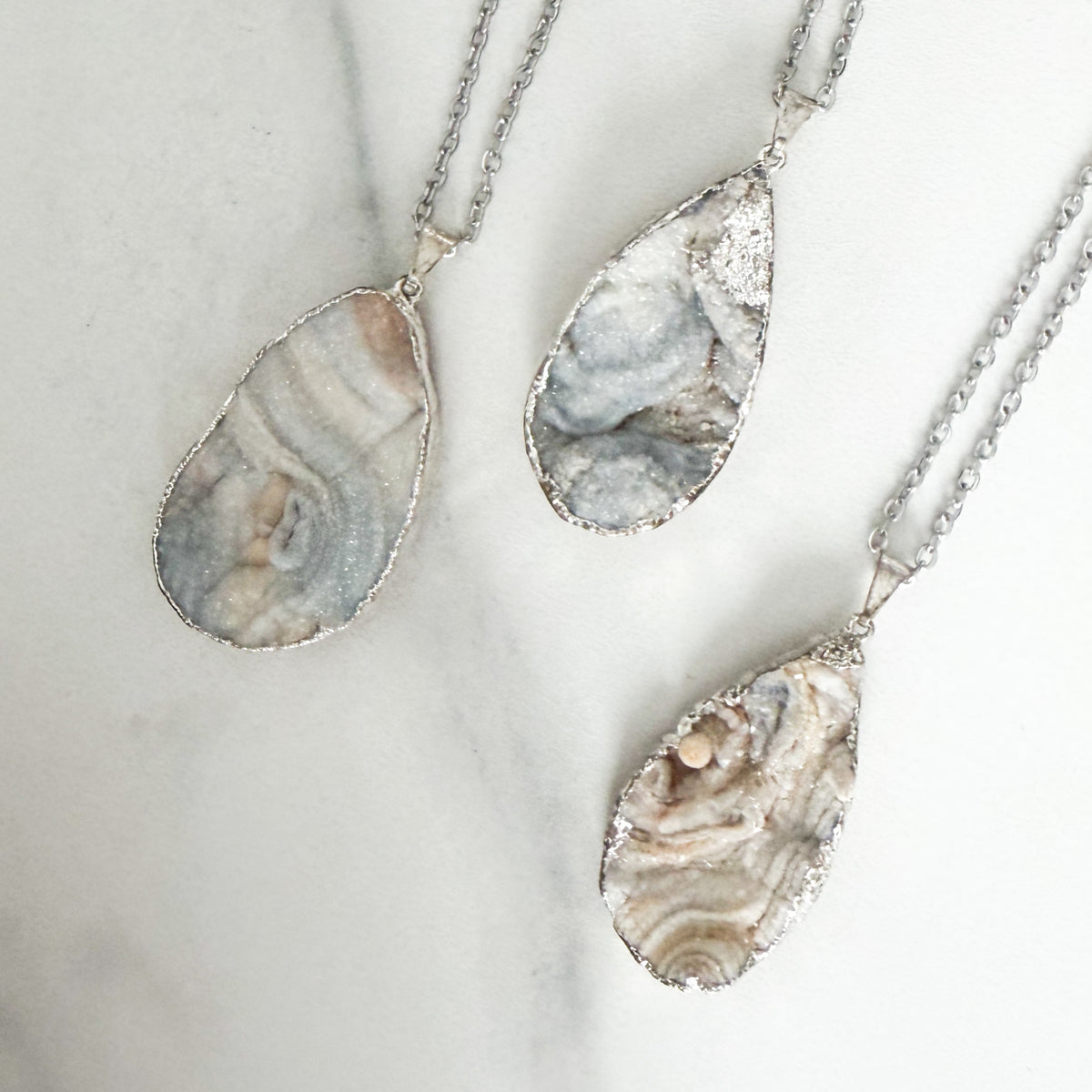Light colored teardrop drusy pendant necklace with sterling silver plated setting on a stainless steel chain.