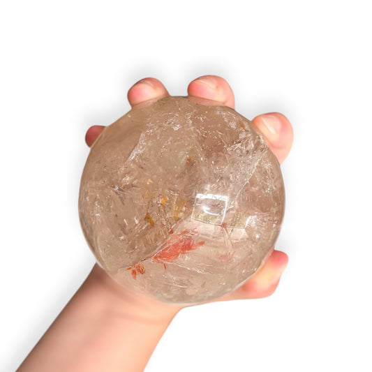 Hand holding a polished Garden Quartz sphere with shamanic inclusions