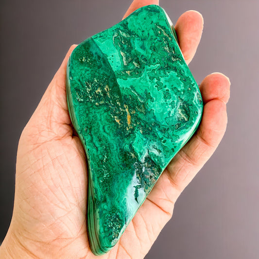 Polished malachite free form held in hand for scale