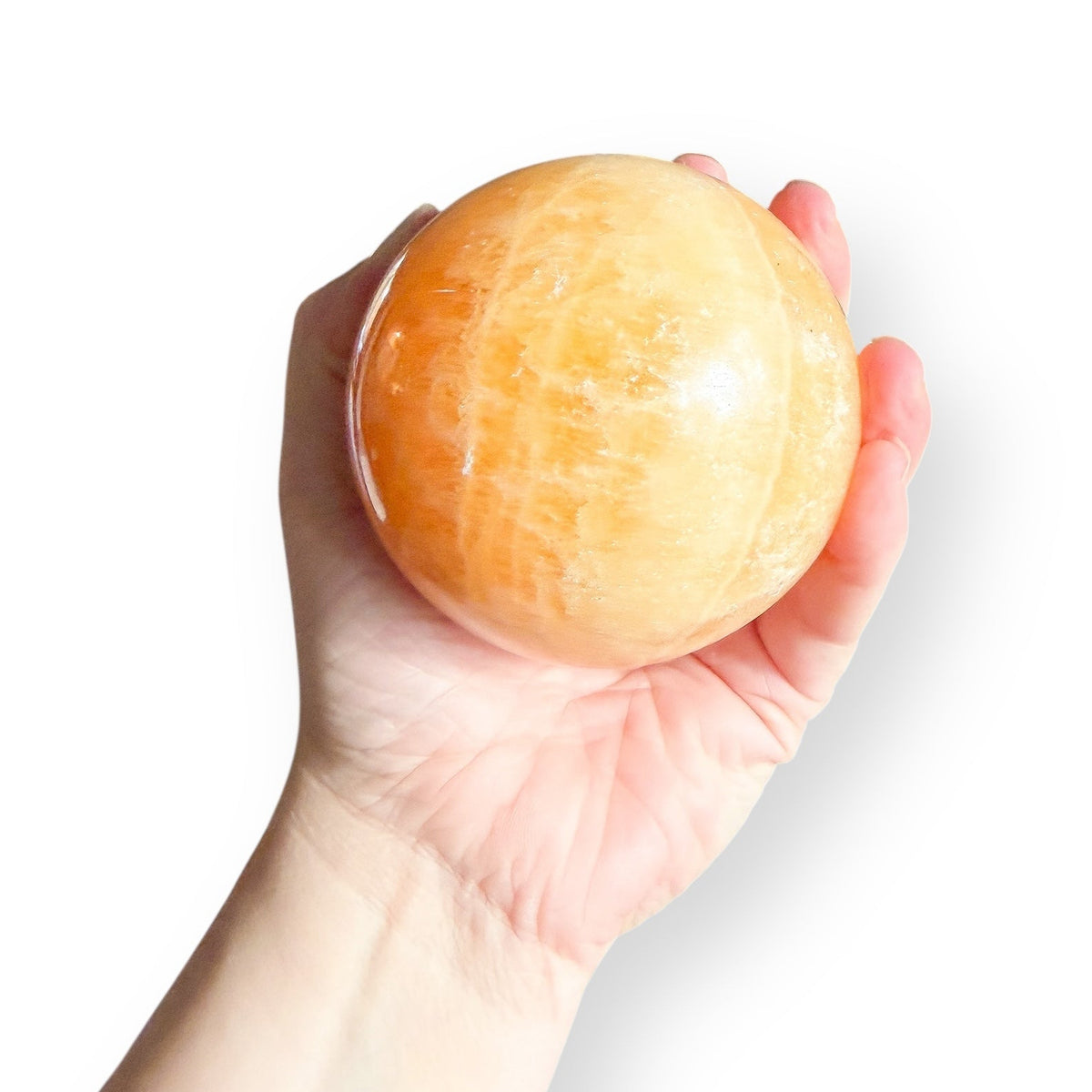 Orange Calcite sphere shown in hand for size reference