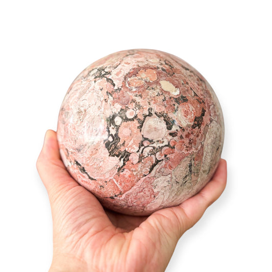 Hand holding Pink Rhodonite sphere for emotional healing
