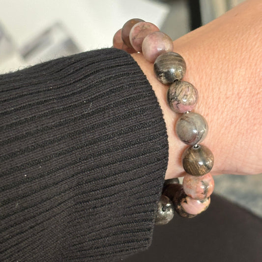 Elegant Rhodonite bracelet styled with gold rings and warm-toned clothing.