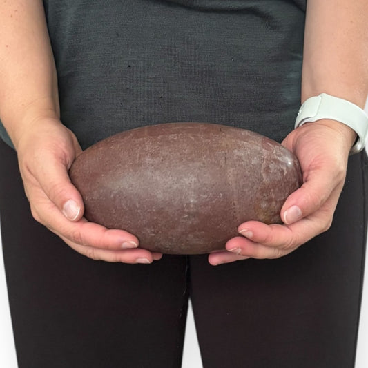 Hand holding the Shiva Lingam stone to show scale and smooth finish