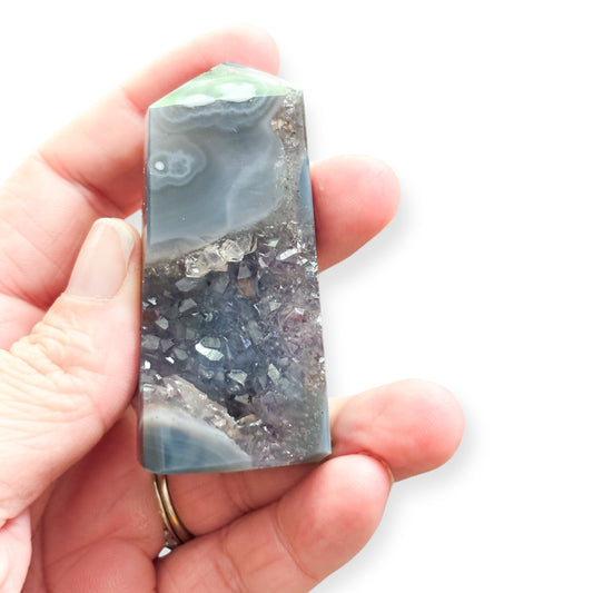 Agate tower with amethyst held in hand to show scale and raw crystal detail