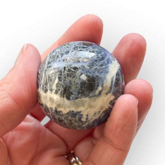 Sodalite crystal sphere resting in hand for size and scale reference.