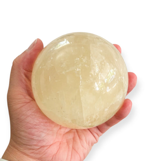 Yellow Calcite crystal sphere in hand showing polished golden surface