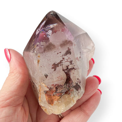 Purple Amethyst Crystal held in a hand with a white background to show size and detail with rainbows.