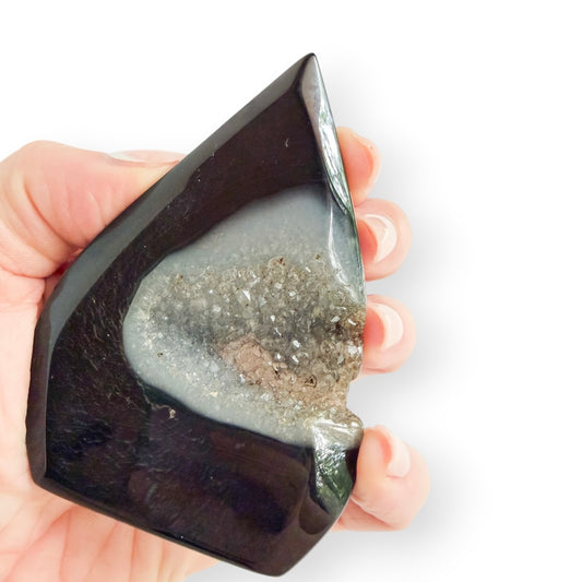 Hand holding a black agate, freestanding teardrop form with drusy accent, showing size and details.