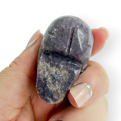 Hand holding a hand carved lepidolite skull showing the bottom details.