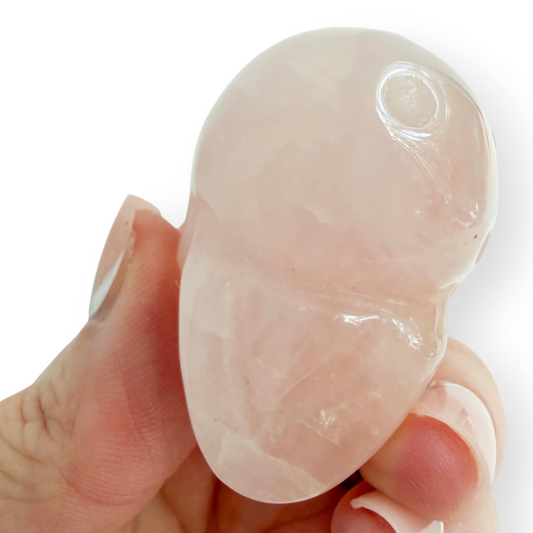 Hand holding A small rose quartz skull to show the base.
