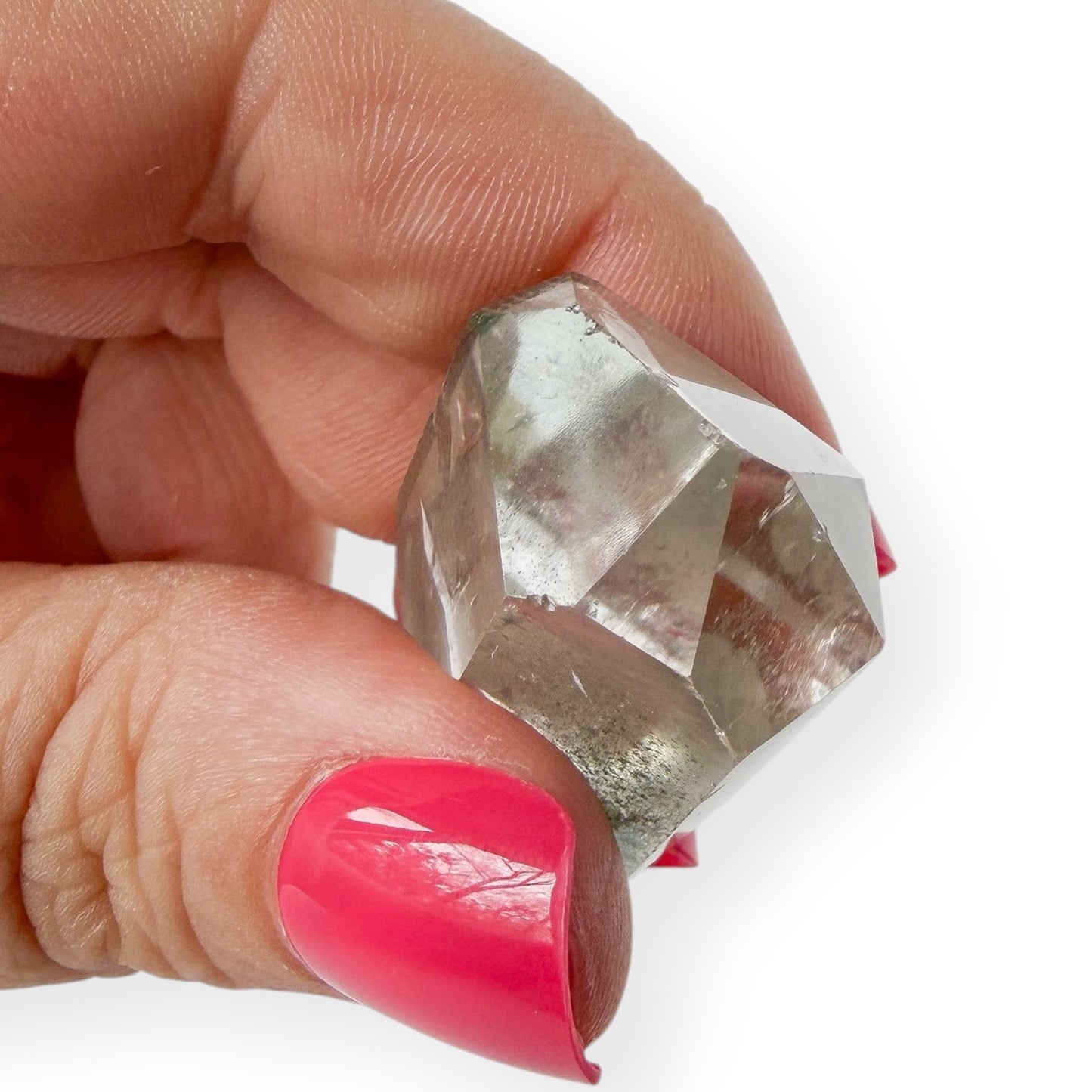 Hand holding a clear crystal showing the point and imperfections with pink nail polish on a white background