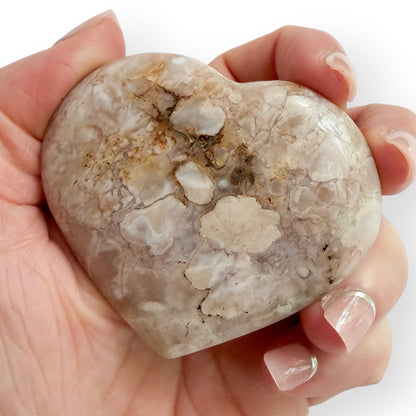 Hand holding     Flower Agate heart with pale pink and cream floral inclusions, natural banding, and polished finish.