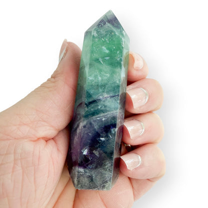 A hand holding a green and purple fluorite obelisk showing details and size.
