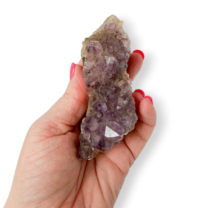 Hand holding an oblong purple amethyst crystal on a white background