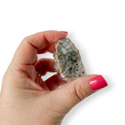 Hand holding an amethyst crystal with a white background showing the details of the bottom of the crystal