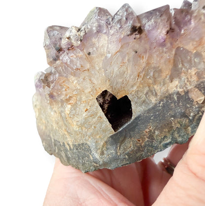 Amethyst crystal held in a hand against a white background with a heart shaped hole