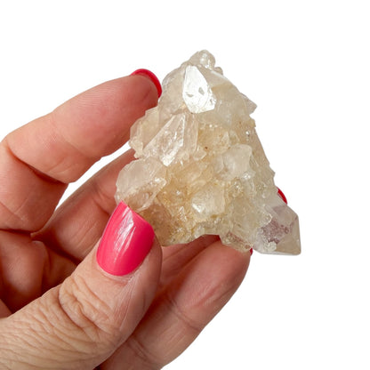 Hand holding a clear crystal rock with pink nail polish on a white background