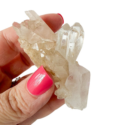 Hand holding a crystal cluster with pink nail polish on a white background