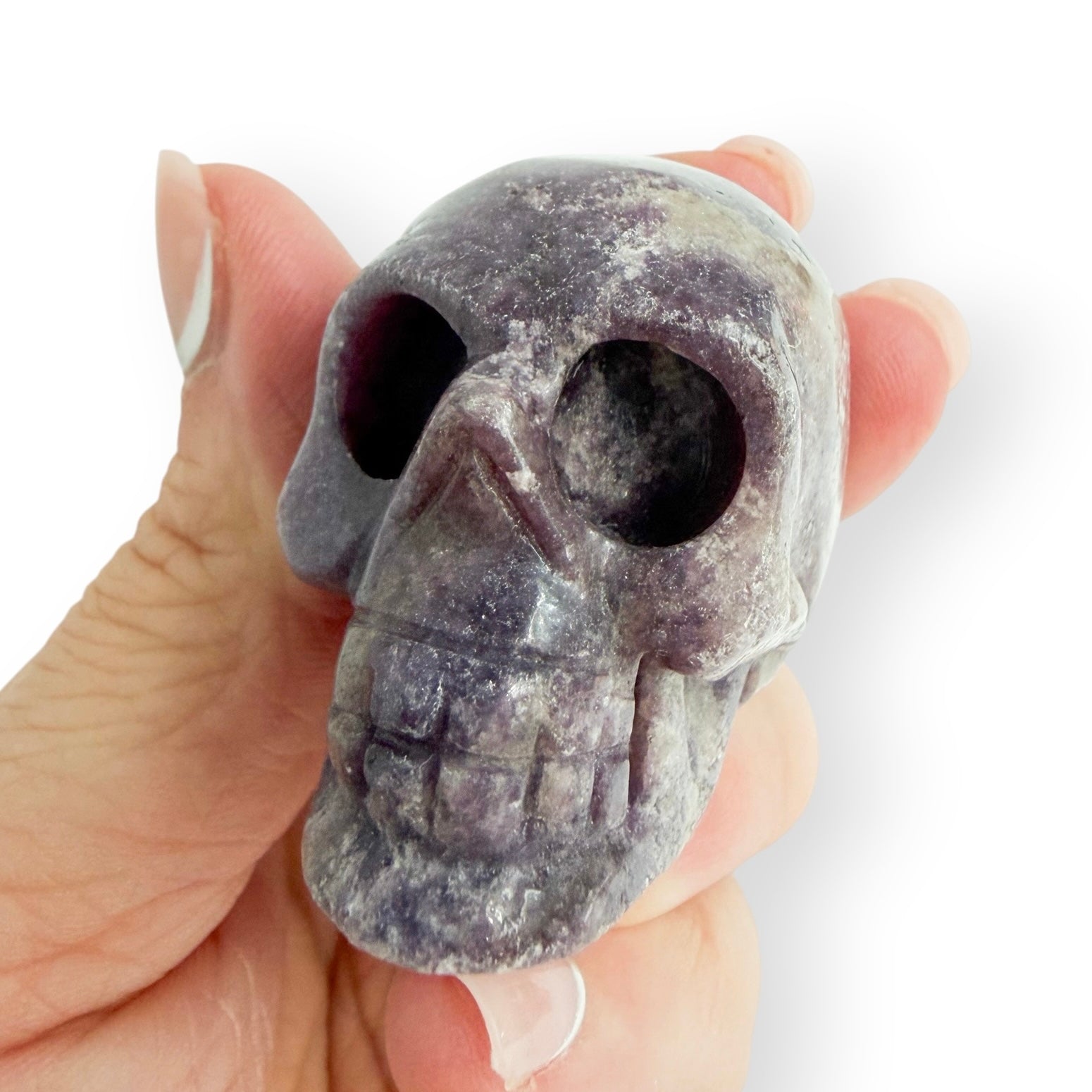 Hand carved purple lepidolite skull in hand, showing the detail and size.