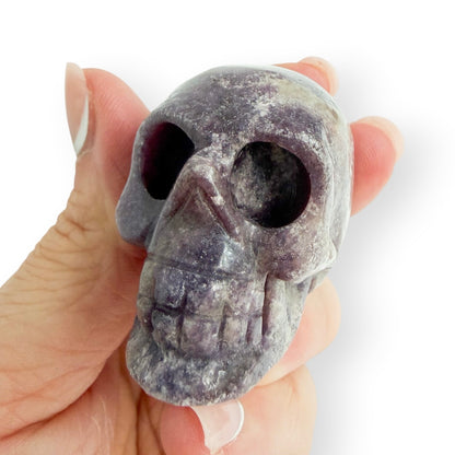 Hand carved purple lepidolite skull in hand, showing the detail and size.