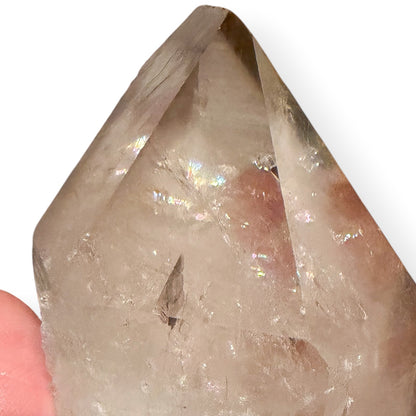Clear crystal point held by a hand on a white background with rainbows