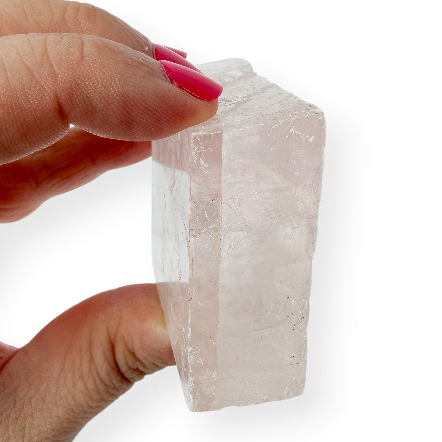 Hand holding a clear optical calcite side view against a white background to show detail