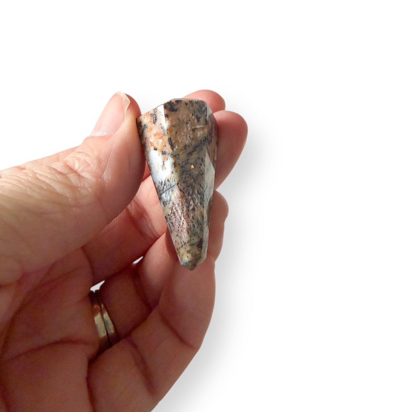 Hand holding a sea jasper pendulum to see detail against a white background