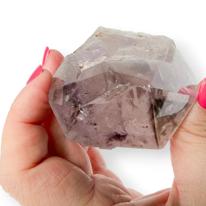 Hand holding a clear crystal with pink nail polish on a white background showing the chips on the tip of the crystal. 