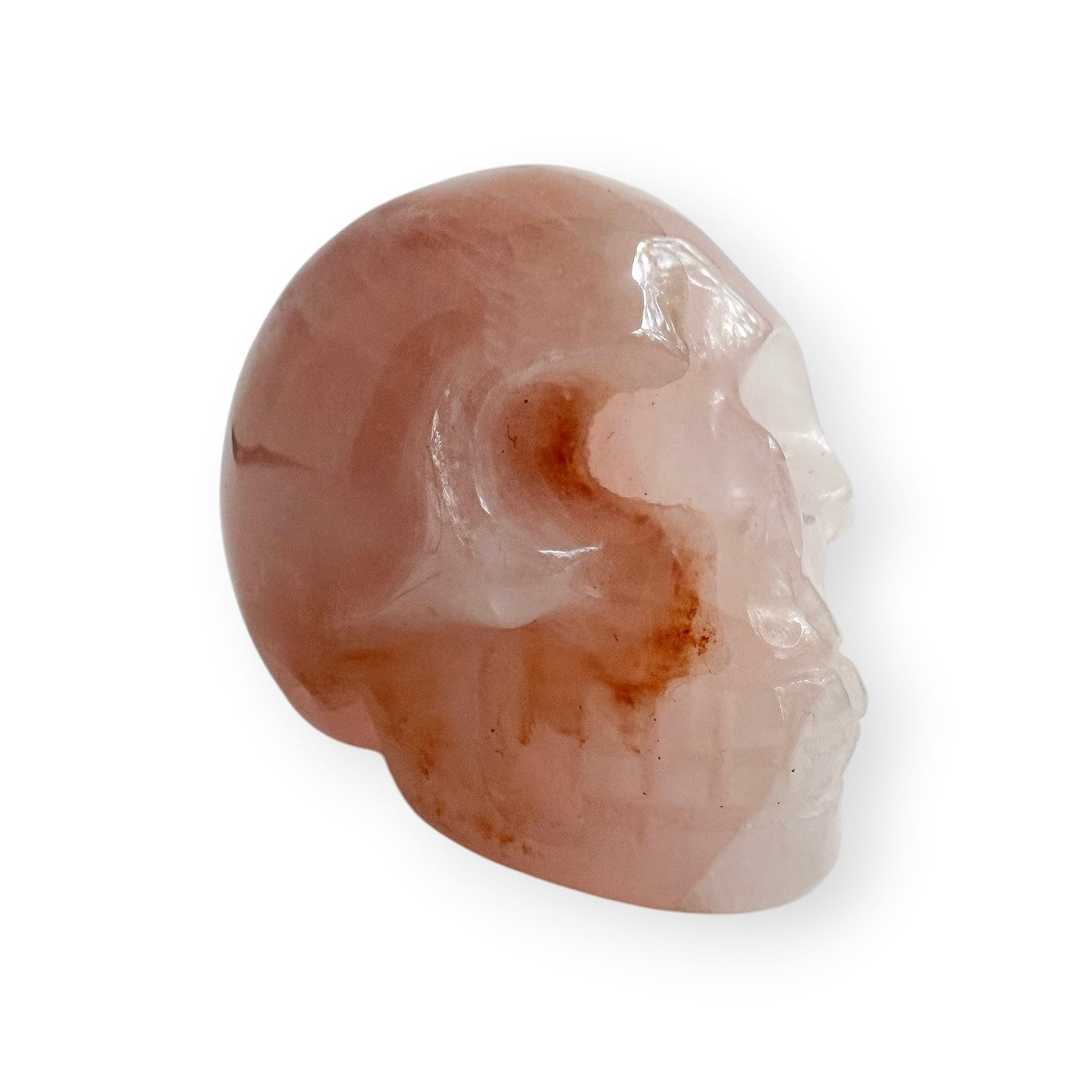 Side view of a rose, quartz hand carved skull on a white background.