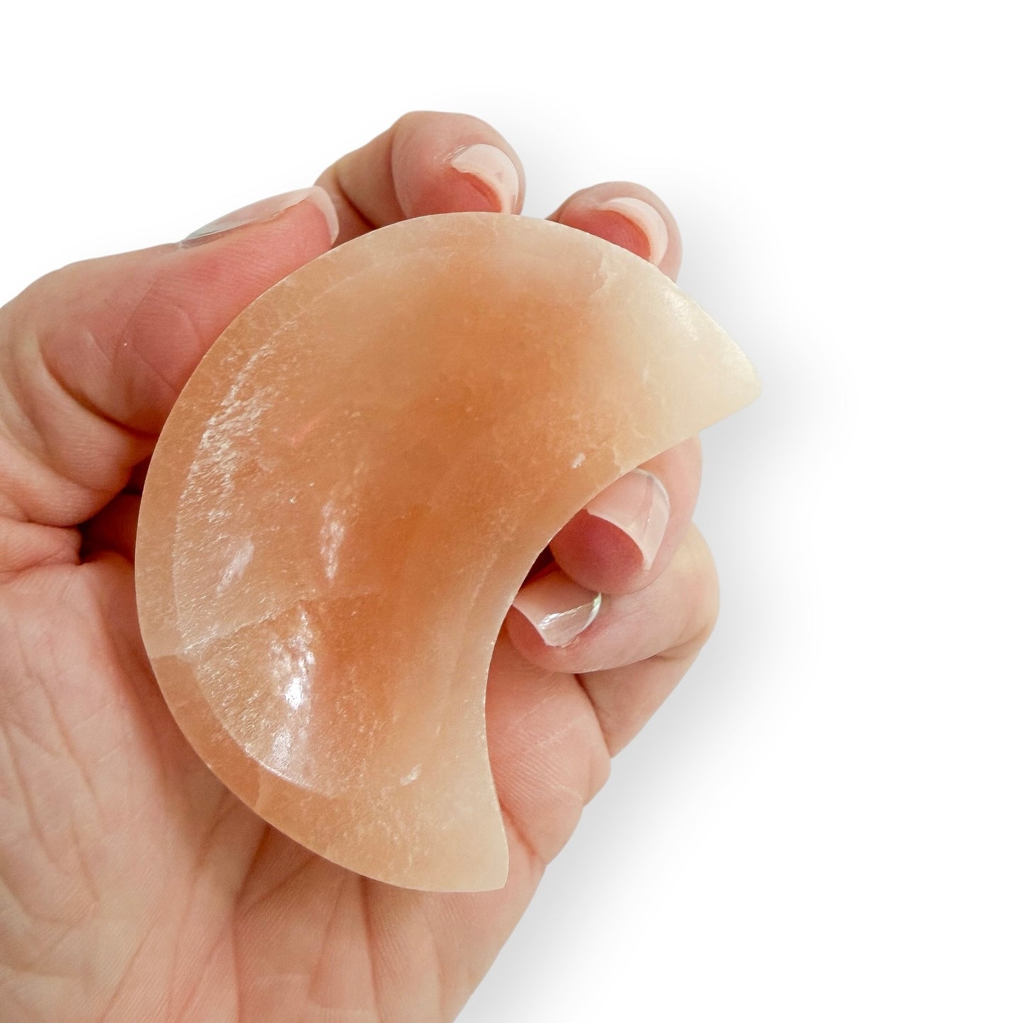 Hand holding small Peach-orange Satin Spar moon-shaped bowl carved from natural crystal with a smooth polished finish.