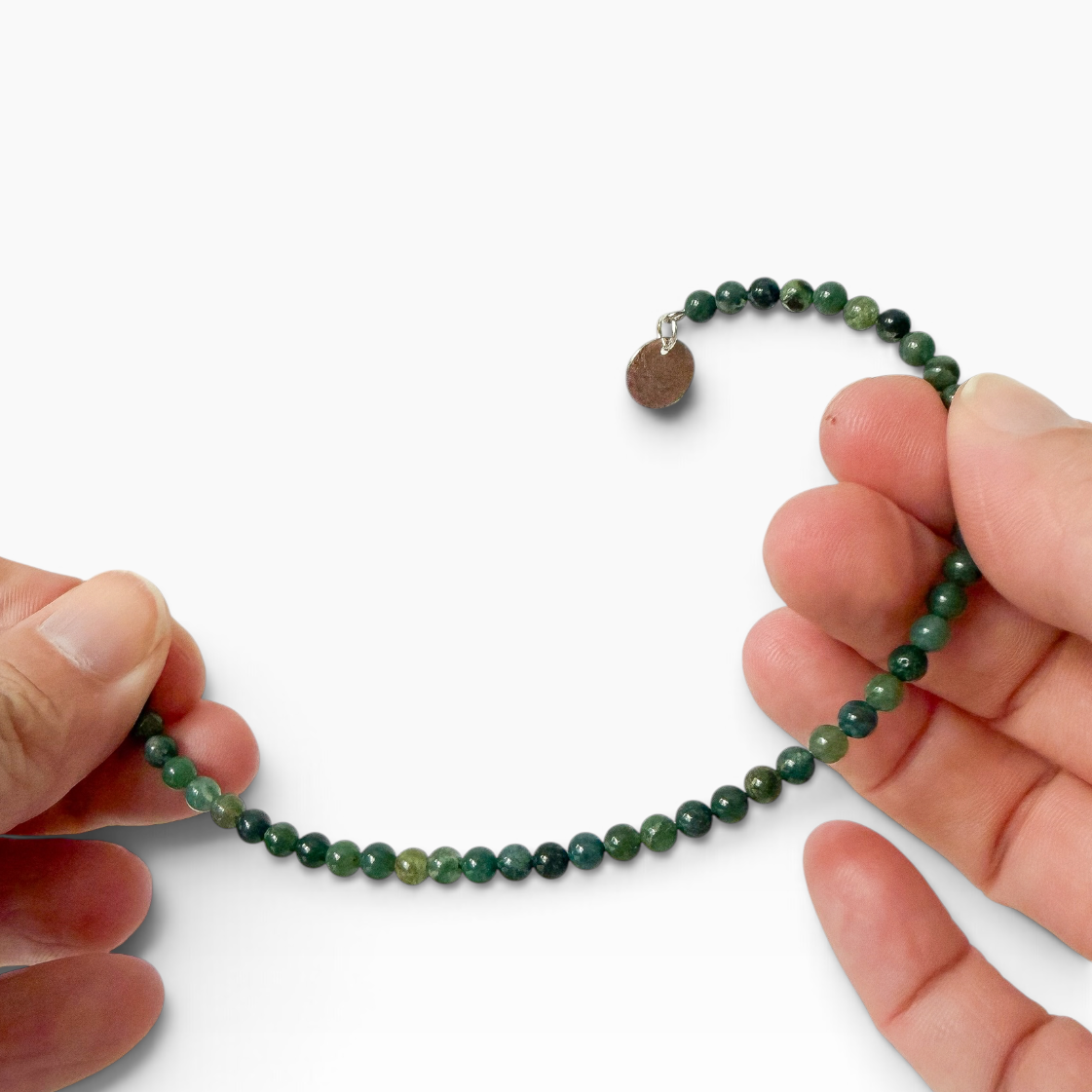 A beaded bracelet made of small green moss agate beads with a small charm, held between two hands against a plain white background.