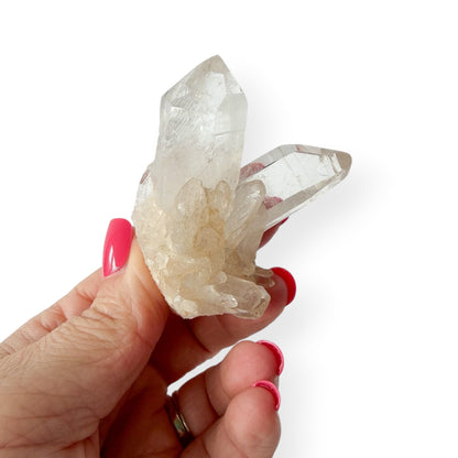 Hand holding a clear crystal with pink nail polish on a white background